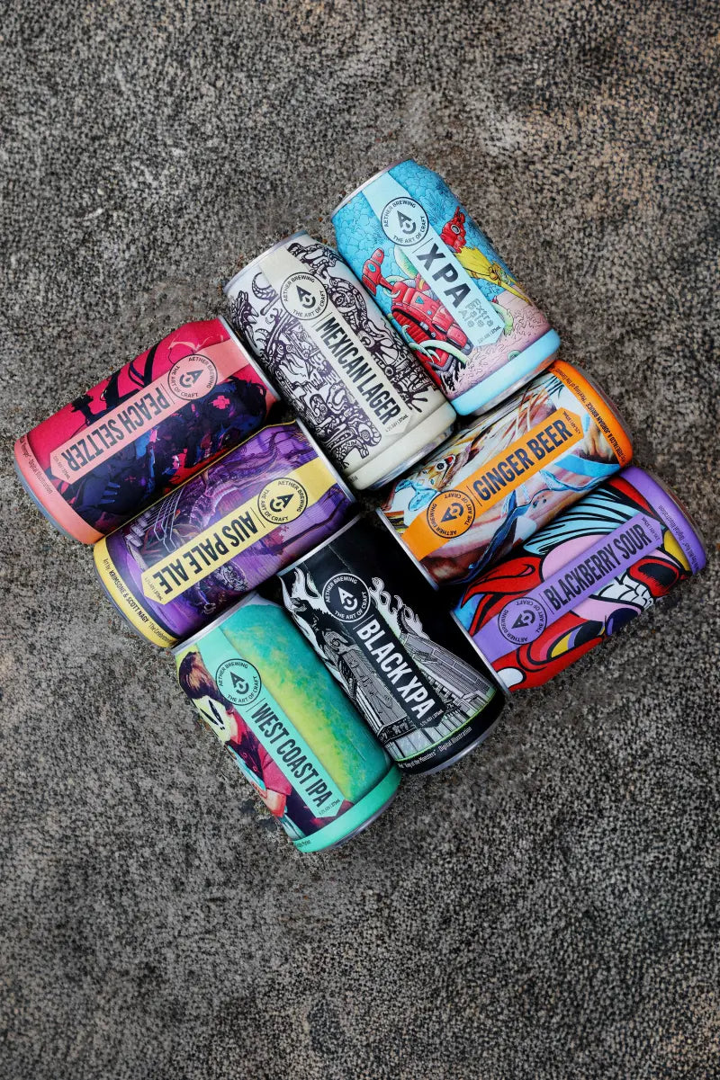 Australian craft brewery, Aether Brewing’s craft beers range laid out in a diamond. The beers, ginger beer and seltzer are grouped in twos: Mexican Lager, Ginger Beer, Australian Pale Ale, Black XPA, Hard Peach Seltzer, Blackberry Sour, XPA and West Coast IPA. The beers are on concrete at their independent, family-owned brewery home in Northgate, Brisbane.