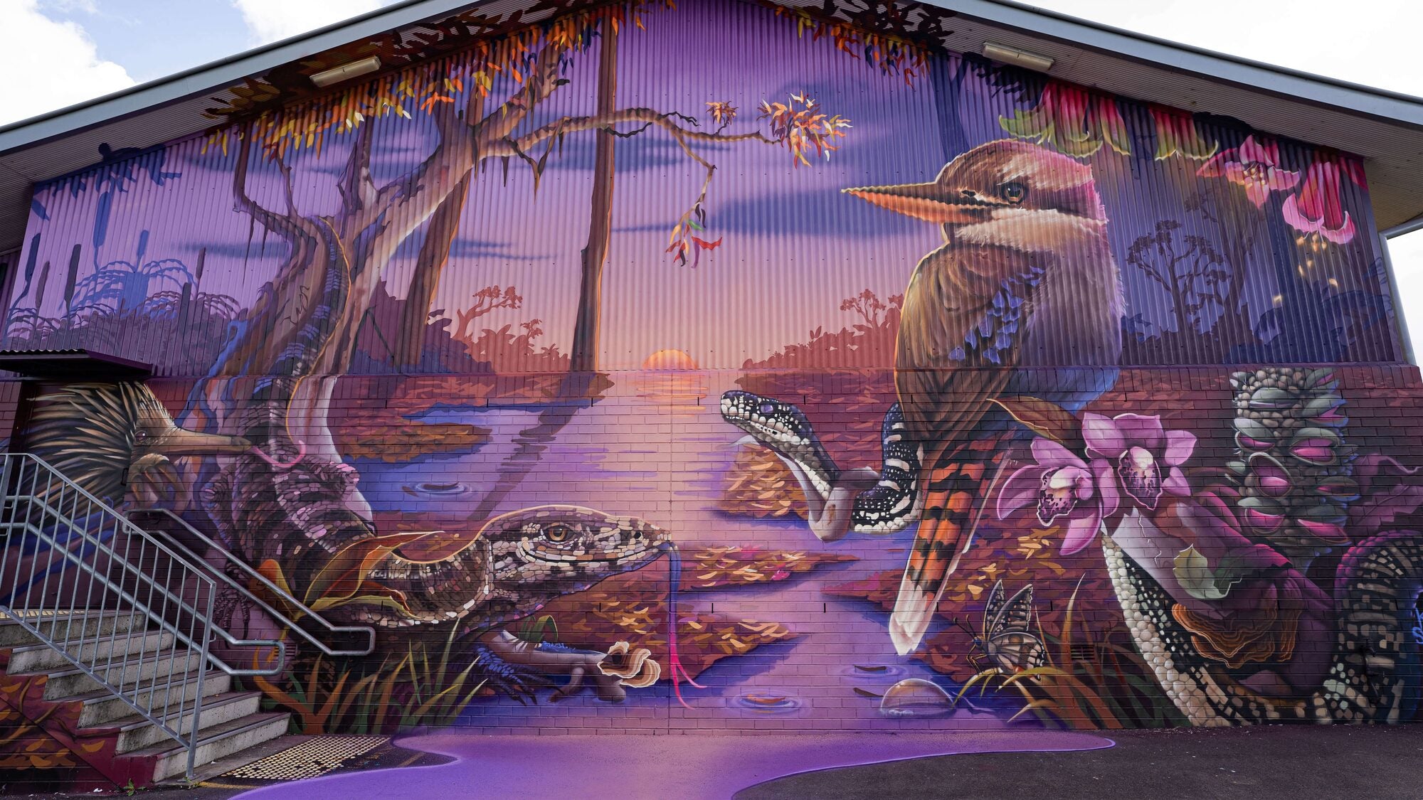Mural 'Celebration of Light' by Krimsone and Scott Nagy showing kookaburra, lace monitor, flowers and waterways in vivid sunset colours, featured by Aether Brewing.